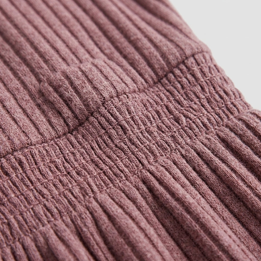 Close-up of a ribbed knit garment in a dusty mauve color, showing the texture and construction details against a light gray background.