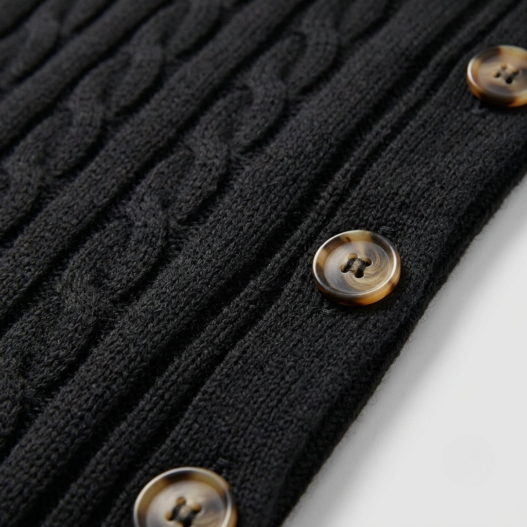 Close-up of a black cable-knit cardigan with three tortoiseshell buttons on a white background.