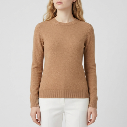 A woman wearing a light brown crewneck knit sweater and white trousers, shown from the chin down against a light gray studio background.