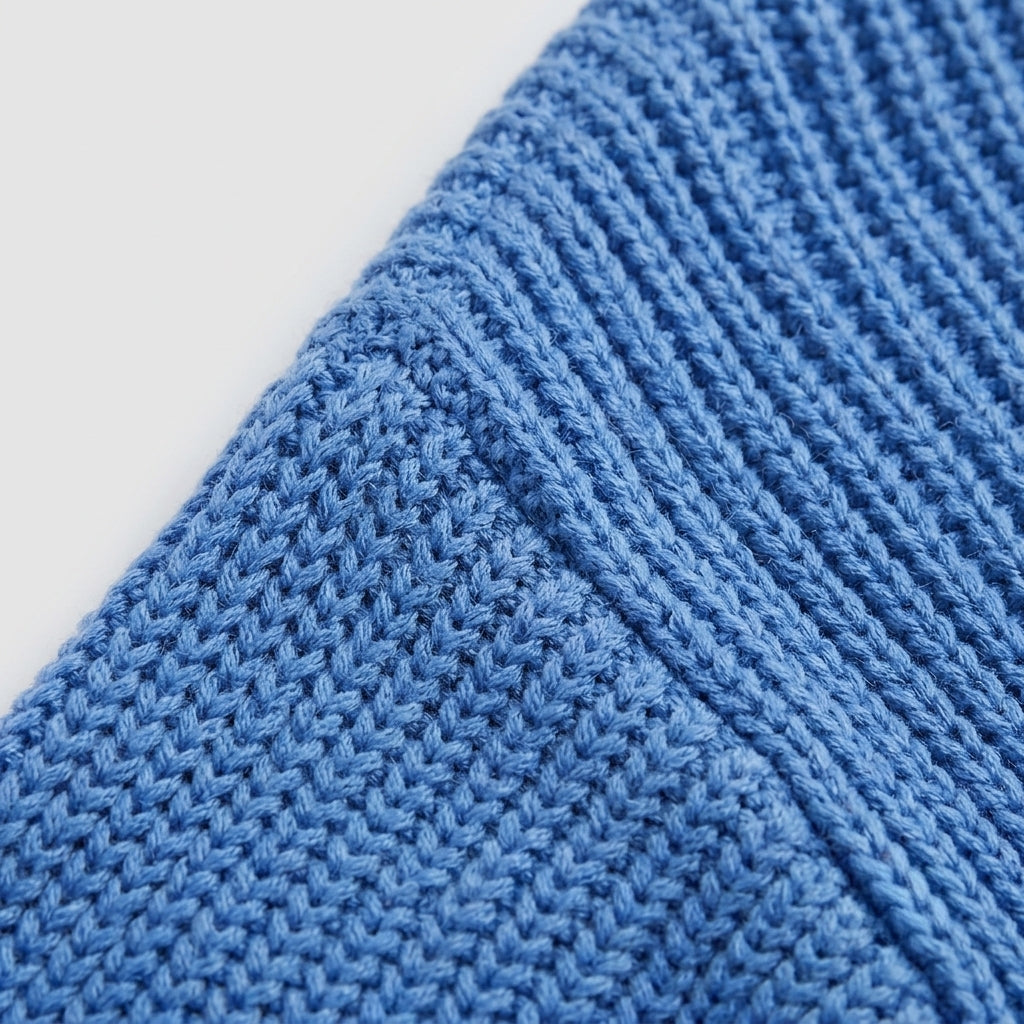 Close-up of a blue knitted fabric with a textured chevron pattern, showing the detailed knit stitches against a plain white background.