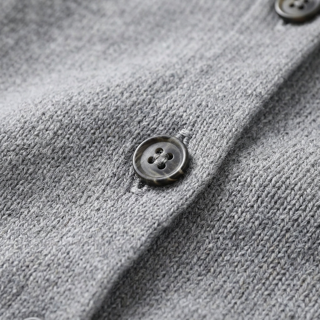 Close-up of a gray knit cardigan or sweater showing the textured fabric and a dark button on the front.