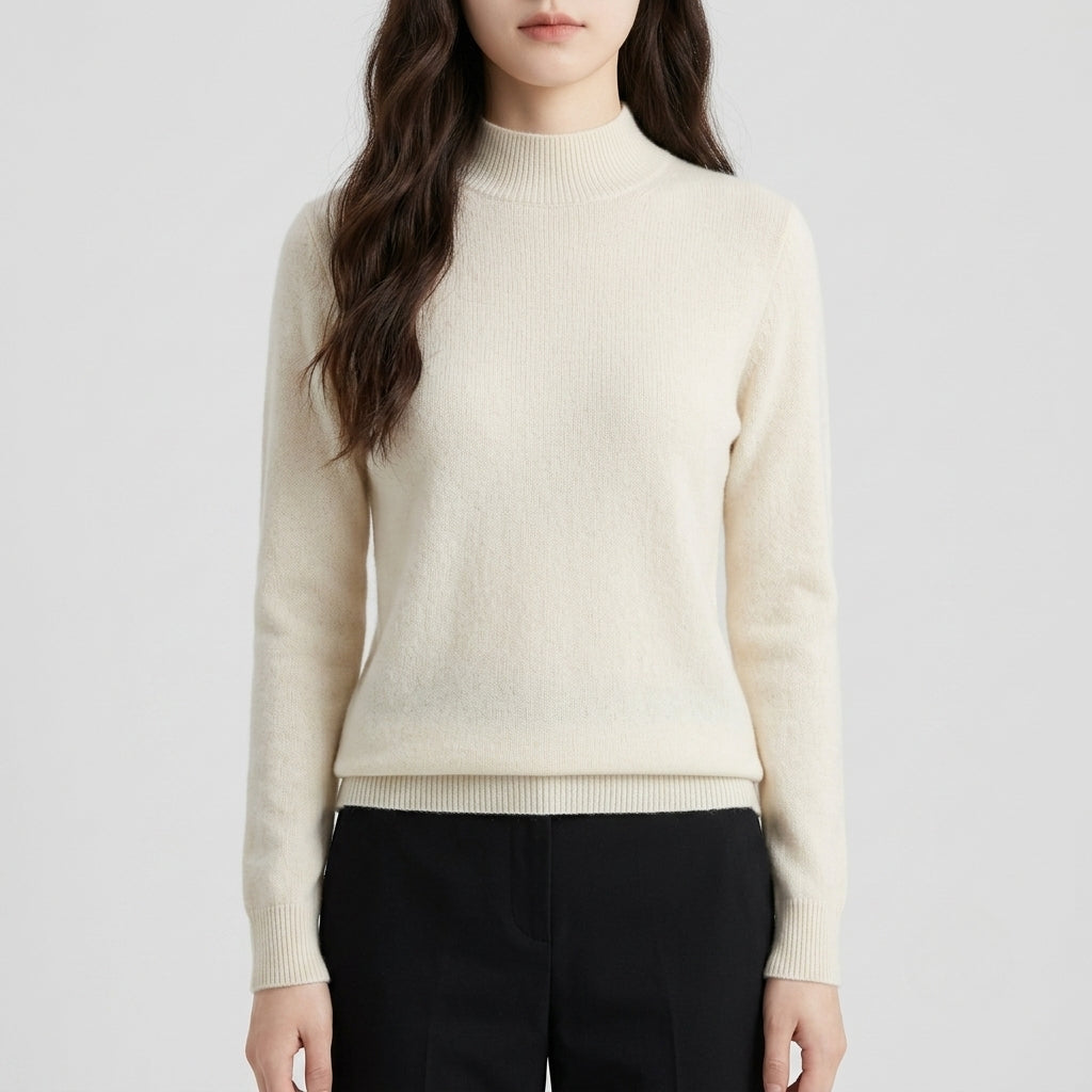 A woman wearing a white-colored knit mock neck sweater and black trousers, shown from the nose down against a light gray studio background.