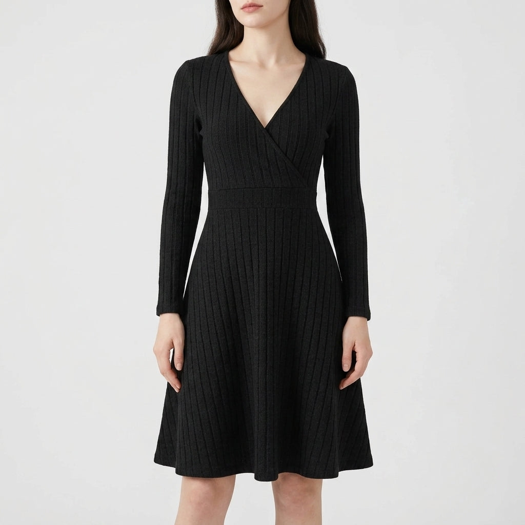 A woman wearing a black ribbed long-sleeve wrap-style dress with a V-neck and flared skirt, photographed against a plain light gray studio background.
